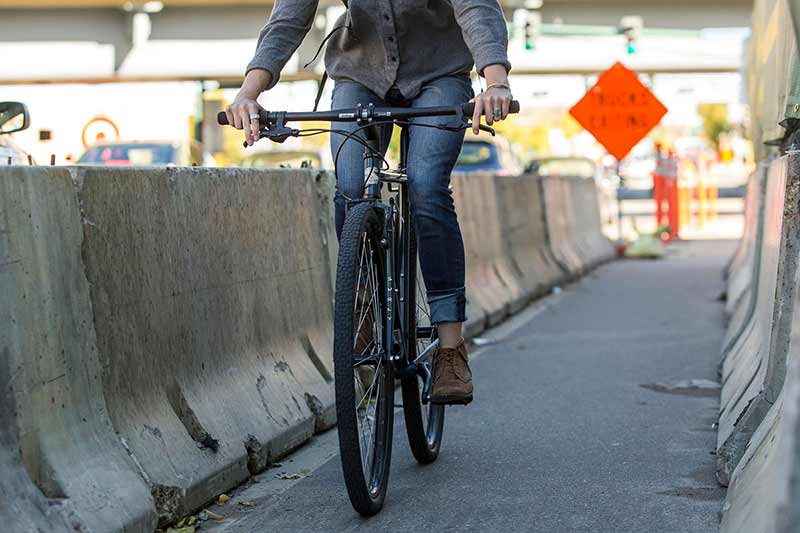 Person riding a bicycle on a city street with barriers and traffic lights in the background